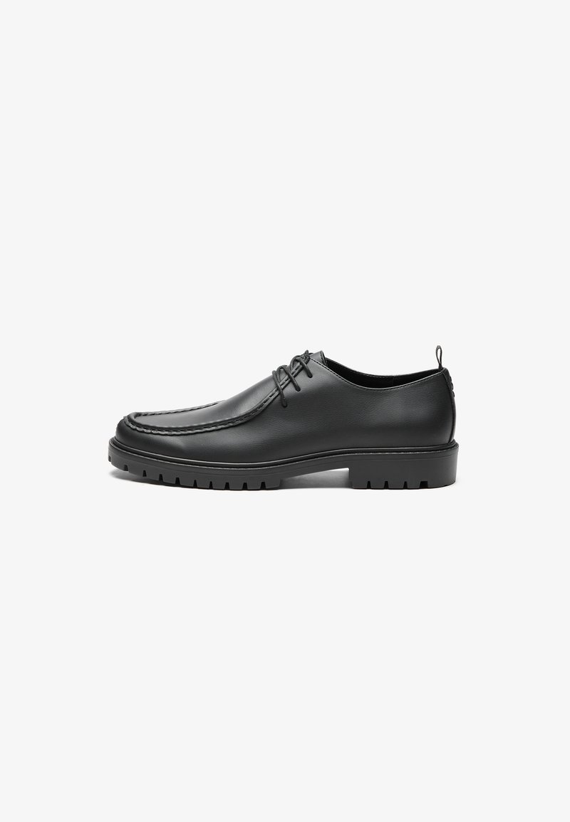Scarpe in pelle nera con finitura liscia, punta tondeggiante e cuciture decorative. Presentano una suola in gomma con scanalature per la trazione e un design con lacci.