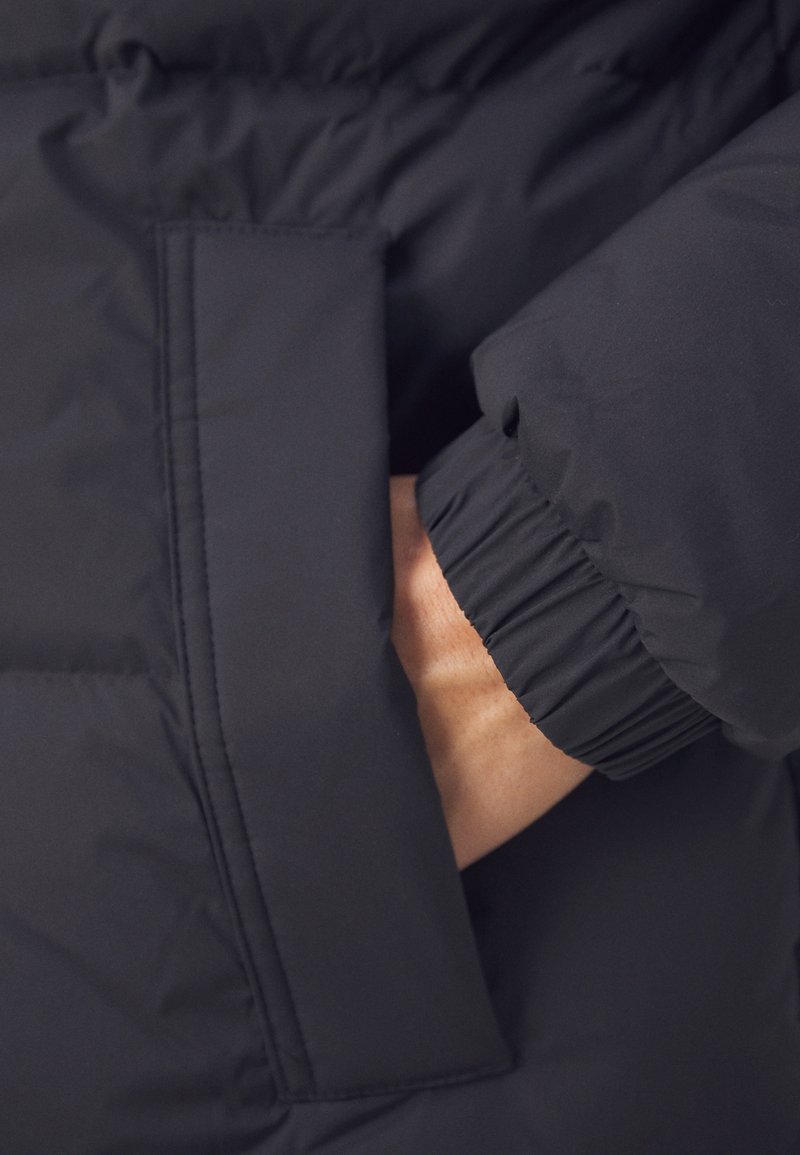 Hand in der elastischen Tasche des gepolsterten schwarzen Winterjackets.