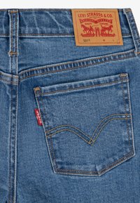 Bolsa trasera de unos vaqueros Levi's 501 azules con costuras naranjas, etiqueta de tela roja y etiqueta de marca de cuero marrón en la cinturilla.