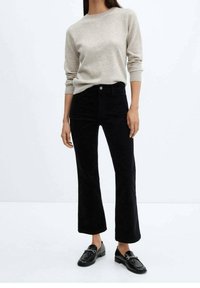 Beige sweater with long sleeves, paired with high-waisted black corduroy flared pants. Black loafers with a chain detail complete the look.
