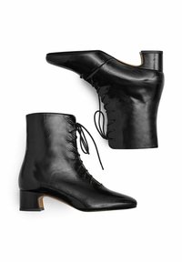 Černé kotníkové boty z pravé kůže se špičatou špičkou, zavazováním vpředu a nízkým blokovým podpatkem. Mají hladkou texturu a elegantní design.