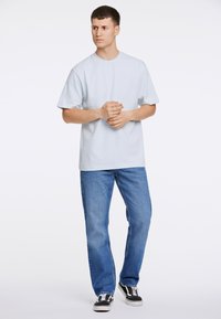 Vaaleansininen puuvillapaita lyhyillä hihoilla, yhdistettynä sinisiin farkkuihin ja mustavalkoisiin lenkkareihin. Minimalistinen muotoilu, ei kuvioita.