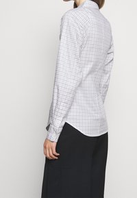 Camisa de manga larga en gris claro con un patrón de cuadrícula, puños abotonados y dobladillo curvado. Confeccionada en un tejido suave y transpirable.
