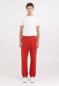 Røde jeans med rett ben laget av bomullstwill, med fem-lommers design og kontraststing, sammen med en enkel hvit t-skjorte og hvite joggesko.