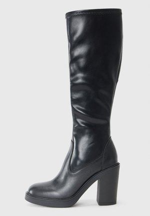 Bota preta até ao joelho, feita de couro liso, com um design elegante, bico quadrado e salto alto grosso para um aumento de altura. Apresenta costuras mínimas.