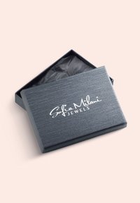 Grå strukturerad smyckeslåda med ett lyftlock, med vit kursiv märkning "Sofia Milani JEWELS" på toppen, fodrad med svart silkespapper inuti.