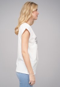 T-shirt blanc à manches courtes, avec un graphique de pissenlit noir. Associé à un jean bleu clair, offrant une coupe décontractée.