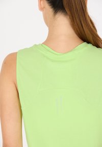 Ärmlös, ljusgrön träningsoberdel i mjukt material med rundad hals, med subtila ventilationsdetaljer på baksidan.