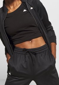 Czarny zestaw sportowy składający się z krótkiego topu i joggerów z regulowanym paskiem w talii. Miękka tkanina z subtelnymi akcentami logo na górze i na nogawce.