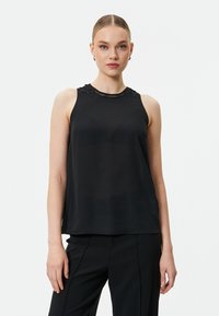 Top nero senza maniche con colletto alto, caratterizzato da dettagli in pizzo intricati e un tessuto liscio e leggero. Abbinato a pantaloni neri su misura.