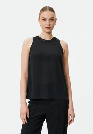 Top nero senza maniche con colletto alto, caratterizzato da dettagli in pizzo intricati e un tessuto liscio e leggero. Abbinato a pantaloni neri su misura.