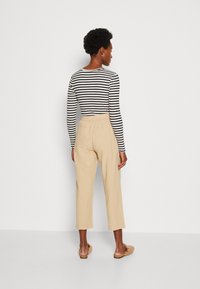 Haut à manches longues rayé avec un design ajusté, associé à un pantalon cropped beige clair. Modèle portant des chaussures à enfiler en fausse fourrure beige.