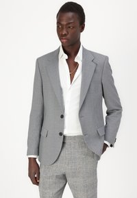 Sacou gri din material texturat, cu rever în formă de zimți, două butoane și buzunare laterale; asortat cu o cămașă albă și pantaloni cu un model.