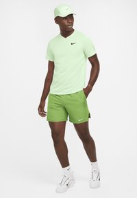 Vihreä Nike lyhythihainen paita ja vihreät shortsit, jotka on yhdistetty yhteensopivaan lippikseen ja valkoisiin lenkkareihin. Yksinkertainen muotoilu, logo rinnassa ja shortseissa.