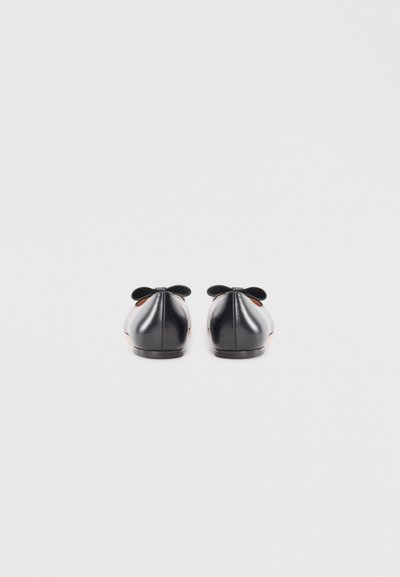 Ballerines noires en cuir avec des bouts ronds, des détails de couture à l'arrière et de petits nœuds décoratifs sur le talon. Texture lisse et design minimaliste.