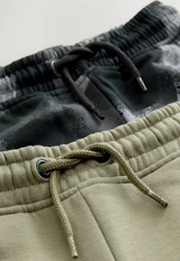 Două perechi de pantaloni de jogging: una neagră cu modele gri și una de culoare verde măslinie. Ambele au talie elastică și detalii cu șnur.