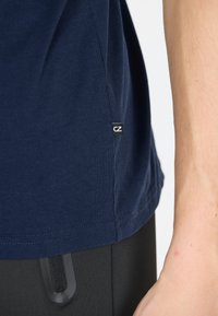 Marinblå bomulls t-shirt med slät textur, sidomärke med "CZ" och korta ärmar, matchad med svarta byxor med synliga fickdetaljer.