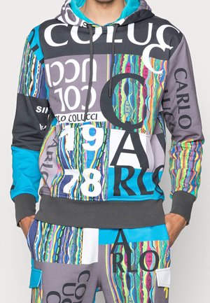 Mehrfarbiger Hoodie und Hose mit auffälliger Grafik, Text „CARLO COLUCCI“, „1978“ und mehrfarbigen vertikalen Streifenmustern an Ärmeln und Oberkörper.