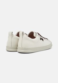 Pair of off-white leather sneakers with dark brown laces, low rubber soles, and a heel pull tab, shown from the back and side angle.