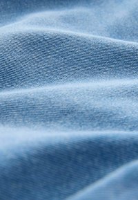 Světle modrý denimbat s hladkou strukturou, který obsahuje jemné vzory tkaní a mírné záhyby vytvářející hloubku.