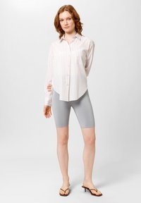 Lichtroze en witte gestreepte overhemd met lange mouwen, gecombineerd met aansluitende grijze fietsshorts en dunne bruine teenslippers.