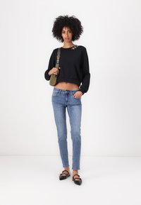 Melna saīsināta džemperis ar apaļu kakla izgriezumu un dekoratīviem elementiem, kopā ar gaiši ziliem šauriem džinsiem un melniem klasiskiem apaviem.