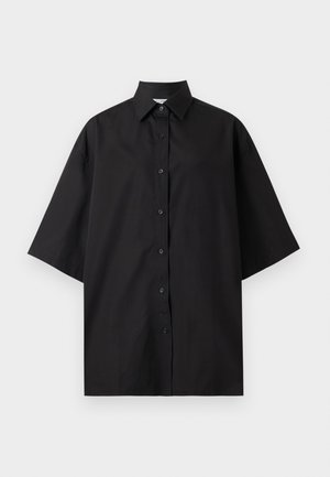 Μαύρο φαρδύ πουκάμισο με κοντά μανίκια, μυτερό γιακά, κουμπιά στο μπροστά μέρος και χαλαρή εφαρμογή, εμφανίζεται σε λευκό φόντο.