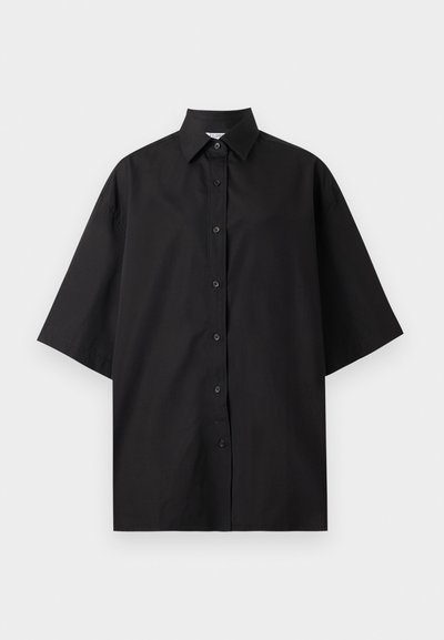 Μαύρο φαρδύ πουκάμισο με κοντά μανίκια, μυτερό γιακά, κουμπιά στο μπροστά μέρος και χαλαρή εφαρμογή, εμφανίζεται σε λευκό φόντο.