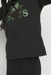 Sudadera de algodón negra con una gran impresión de logotipo de camuflaje. El diseño tiene un corte holgado y mangas largas, con capucha ajustable con cordón.