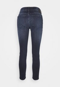 Dark blue skinny jeans with a smooth texture, featuring a mid-rise waist, two back pockets, and a small black leather patch on the waistband.