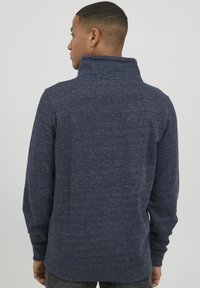 Sötétkék, hosszú ujjú pulóver magas gallérral, texturált szövettel, slim fit szabással, bordázott mandzsettákkal és hemmel, hátulról nézve.