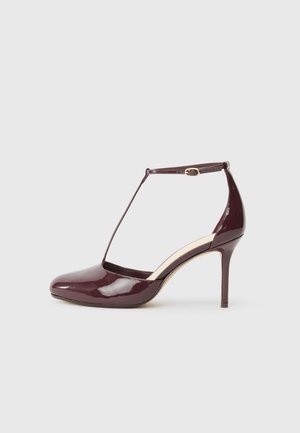 Burgundy patent leather high-heeled shoe with pointed toe, ankle strap buckle, and T-strap detail on a neutral background.