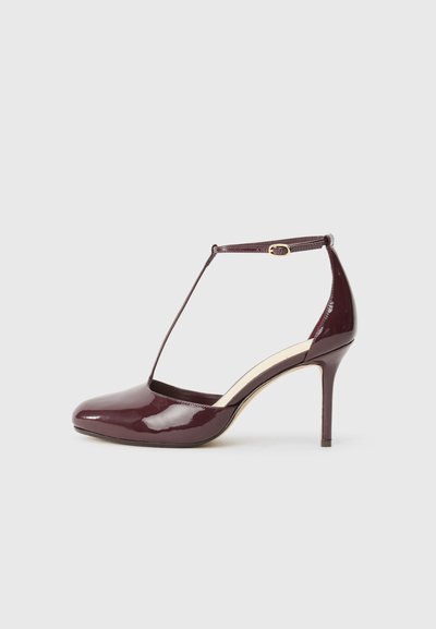 Chaussure à talon haut en cuir verni bordeaux avec bout pointu, boucle sur la bride de cheville et détail de bride en T sur fond neutre.