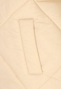 Bézs színű steppelt anyag, középen téglalap alakú párnázott fogantyúval, amely finoman kiemelkedő textúrát hoz létre.