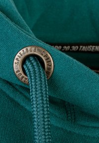 Teal hoodie fabric with a braided drawstring and a metal grommet labeled "SPITZBUB." Close-up detail emphasizes texture and craftsmanship.