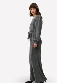 Robe longue métallique grise avec un décolleté en V profond, des manches longues bouffantes et une ceinture nouée à la taille. Présente une silhouette fluide et une texture douce.