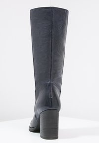 Botte noire en cuir montant jusqu'au genou, à texture lisse, embout carré et talon épais, présentant une couture verticale à l'arrière.