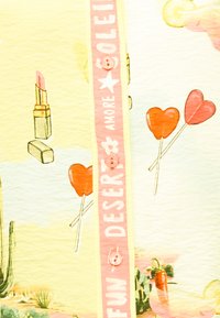 Κίτρινο ύφασμα με ροζ λωρίδα με κουμπιά που γράφει «FUN DESERT AMORE SOLEIL», διακοσμημένο με κραγιόν, κόκκινα γλειφιτζούρια σε σχήμα καρδιάς, κάκτους και φέτες λεμονιού.