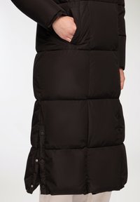 Czarna kurtka puchowa z pikowanym wzorem, posiadająca boczne kieszenie i zatrzaski na dole, wykonana z gładkiego, wodoodpornego materiału.