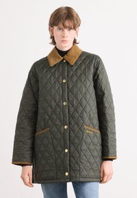 Gequilted groene jas met een bruine suède kraag en afwerking, voorzien van gouden knopen en twee voorzakken, gemaakt van textiel met textuur.