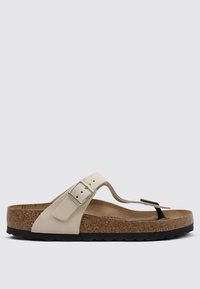 Sandalo a infradito beige chiaro con soletta in sughero, suola in gomma nera e una fibbia metallica decorativa. Materiale morbido con una forma sagomata.