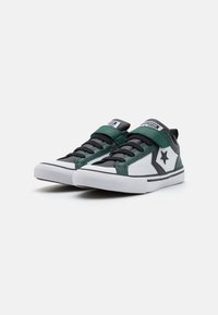 Zapatillas negras, verdes y blancas con lengüeta acolchada, cierre de cordones y velcro, que presentan un logo de estrella y suelas de goma texturizadas.