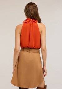 Top rosso con colletto halter e scollatura arricciata abbinato a una gonna A-line color sabbia con vita media e texture liscia.