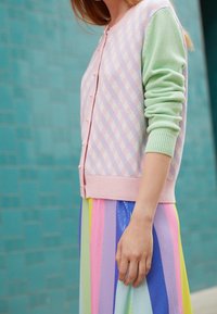 Pastellrosa och grön cardigan med rutig mönstring, små knappar och ribbade ärmar, tillsammans med en flerfärgad randig kjol.