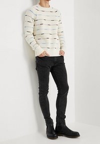 Maglione crema con righe orizzontali multicolori, abbinato a jeans neri aderenti e stivaletti neri. Tessuto liscio e design a coste.
