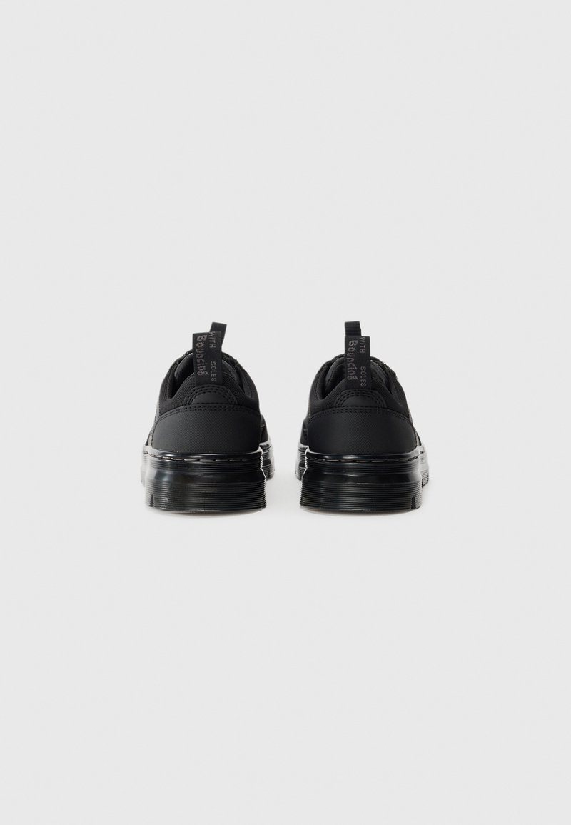 Une paire de chaussures décontractées noires avec des semelles translucides épaisses, vues de l'arrière sur un fond blanc uni.