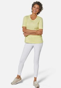 Hellgelbes kurzärmliges T-Shirt, kombiniert mit weißen, eng anliegenden Hosen und beigen Sneakers. Das Material scheint weich zu sein; der Schnitt ist lässig und entspannt.