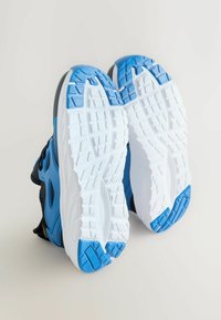 Baskets de sport noires et bleues avec des semelles texturées, dotées d'une semelle intermédiaire blanche et de détails d'accent bleu sur le talon et la semelle.