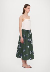 Fustă midi verde cu flori, cu talie elastică și detalii cu fundiță, asortată cu un top alb din satin cu accente brodate. Sandalele completează look-ul.