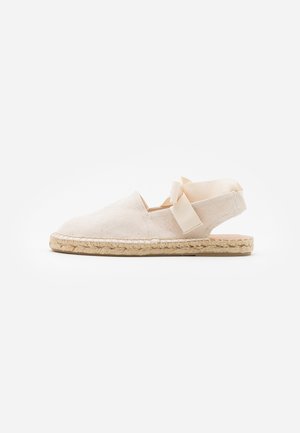 Beige canvas espadrille with a jute sole, featuring a rear strap and ribbon accent. Simple design with rounded toe and casual style.